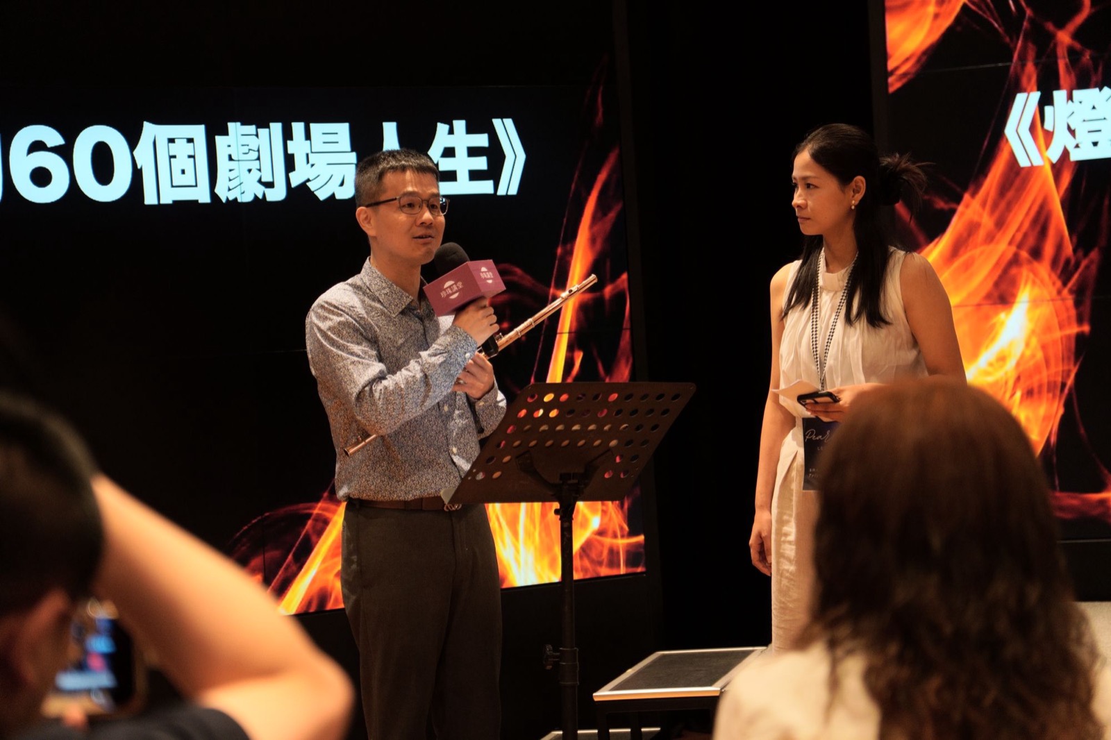 林家驊長笛老師在珍珠講堂講座現場手持長笛演奏，與主持人在台上對談